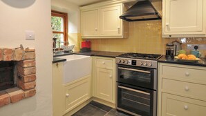 Une cuisine avec une cheminée en briques, une cuisinière à gaz, un four et une horloge au mur.
