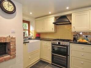 A kitchen with a brick fireplace, a gas stove, an oven, and a clock on the wall. - Jolly Crabber (St Austell)