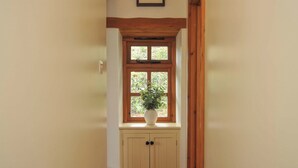 Un couloir avec une porte en bois, une fenêtre ornée d’une plante et un cadre photo accroché au mur.