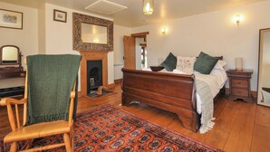 Une chambre à coucher avec un lit en bois, une chaise verte, une cheminée et un grand miroir.