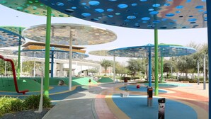 Une aire de jeux avec des structures colorées, un espace de repos abrité et un chemin.
