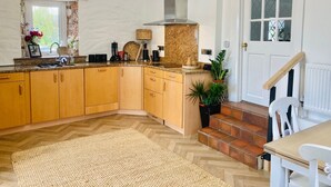 Une cuisine avec des meubles de rangement en bois, un parquet en chevrons, un dosseret en chevrons et une plante en pot.