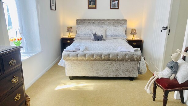 Une chambre à coucher comprenant un lit, deux lampes de chevet, une commode, une chaise et une fenêtre avec des rideaux.