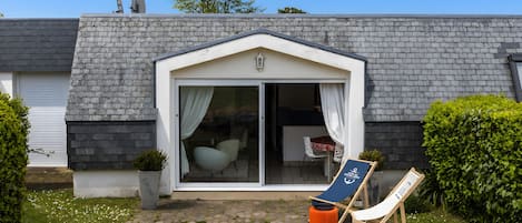 Un edificio con fachada de ladrillo, puerta de vidrio, un pequeño patio con una silla y una mesa, y un cartel.
