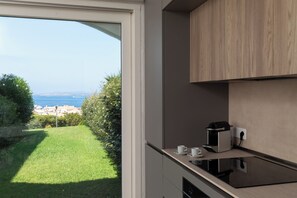 Een moderne keuken met een inbouwoven, een koffieapparaat en uitzicht op een groen gazon en verre gebouwen.