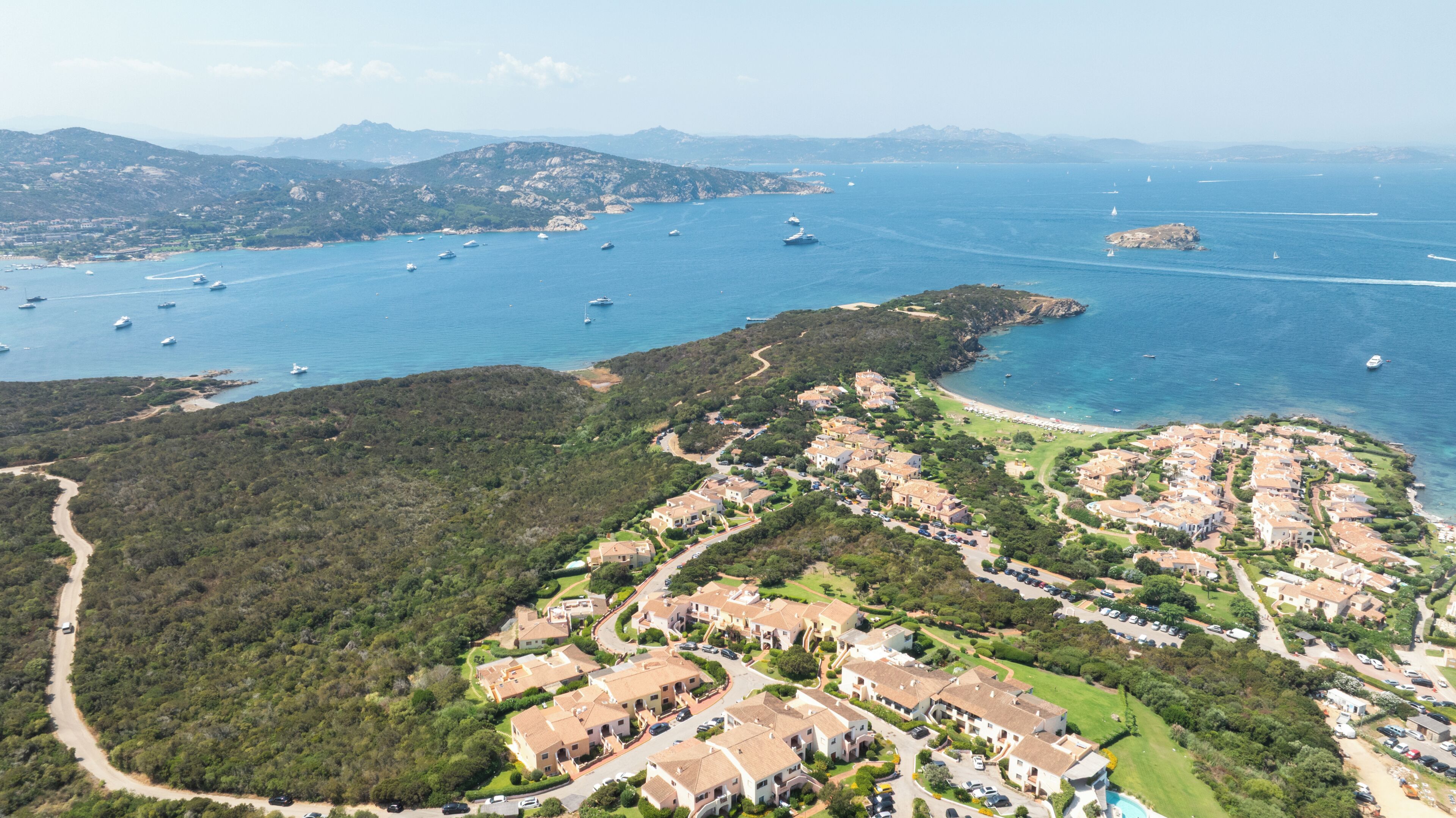 An aerial view of a coastal residential area with houses, roads, and boats in the water.