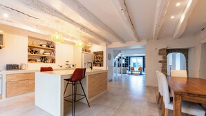 Een moderne keuken met een centraal eiland, houten barstoelen en een eethoek met een houten tafel en stoelen.