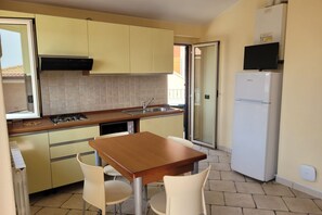 A compact kitchen with a dining table and chairs, a built-in oven, and a refrigerator. - Homiday - The Village, Two Bedroom Apartment with Sea View (Tortoreto)