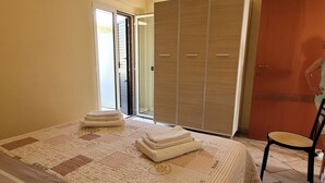 Quarto com cama, cadeira, guarda-roupa e porta que dá para o exterior.