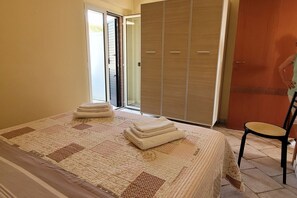 A bedroom with a bed, a chair, a wardrobe, and a door leading outside. - Homiday - The Village, Two Bedroom Apartment with Sea View (Tortoreto)