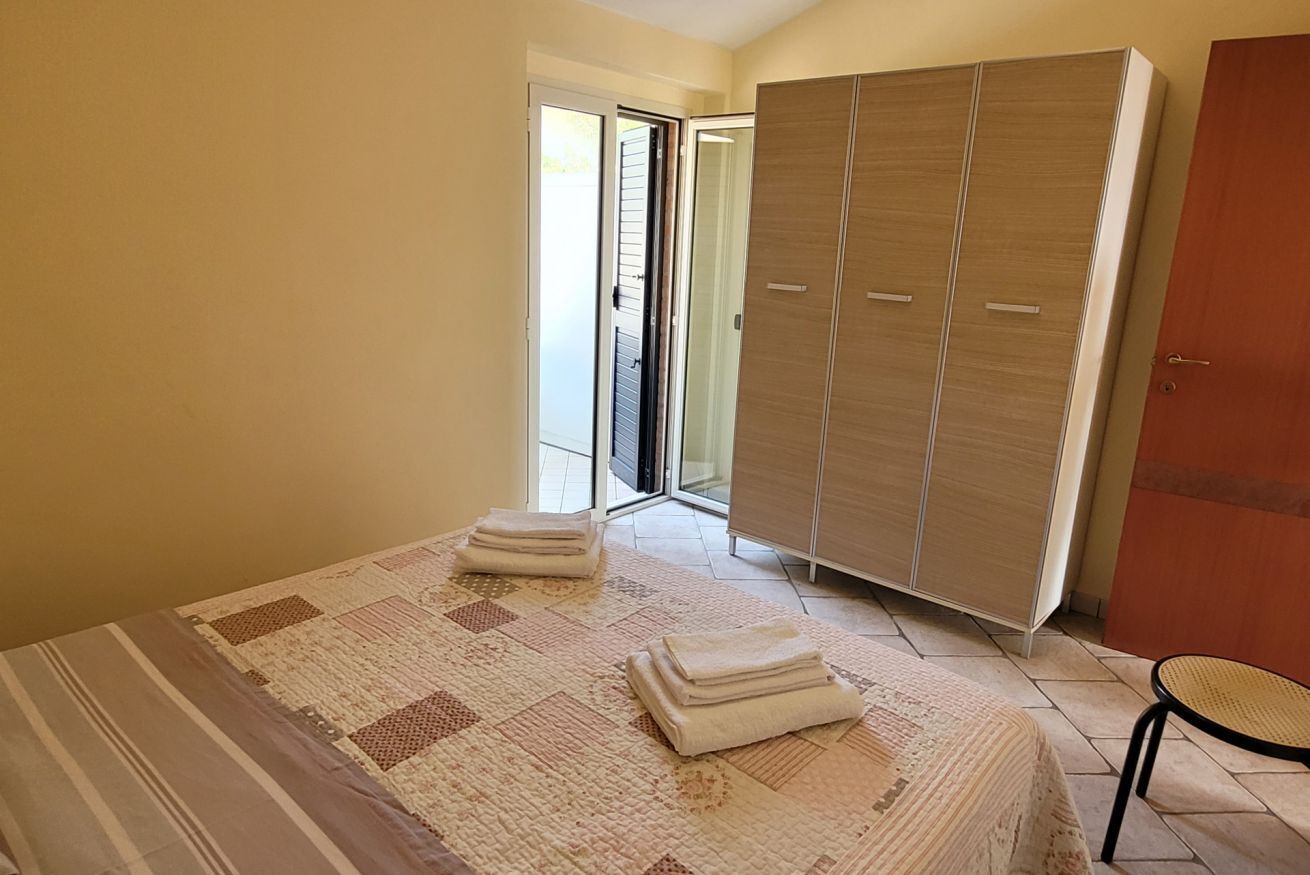 A bedroom with a bed, a wardrobe, a chair, and a sliding glass door leading to a balcony.