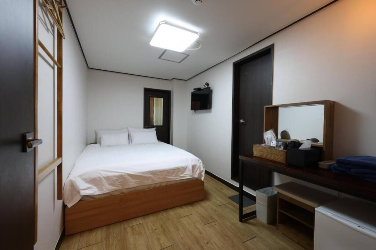 A bedroom with a bed, a desk, a mirror, a wardrobe, and a ceiling light.