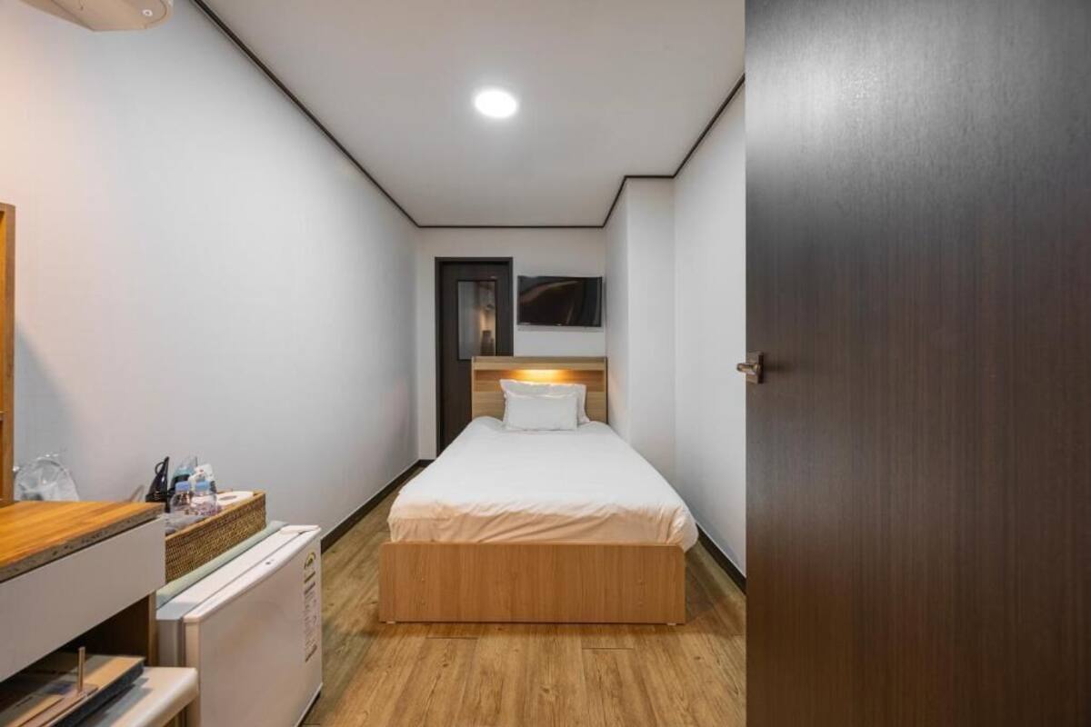 A bedroom with a bed, a dresser, a mirror, a TV, and a door.