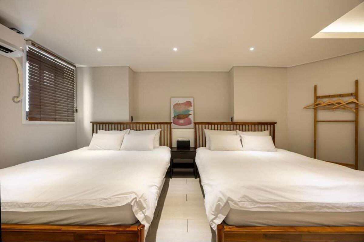 A room with two single beds, a wooden headboard, a small table, and a wall-mounted coat rack.