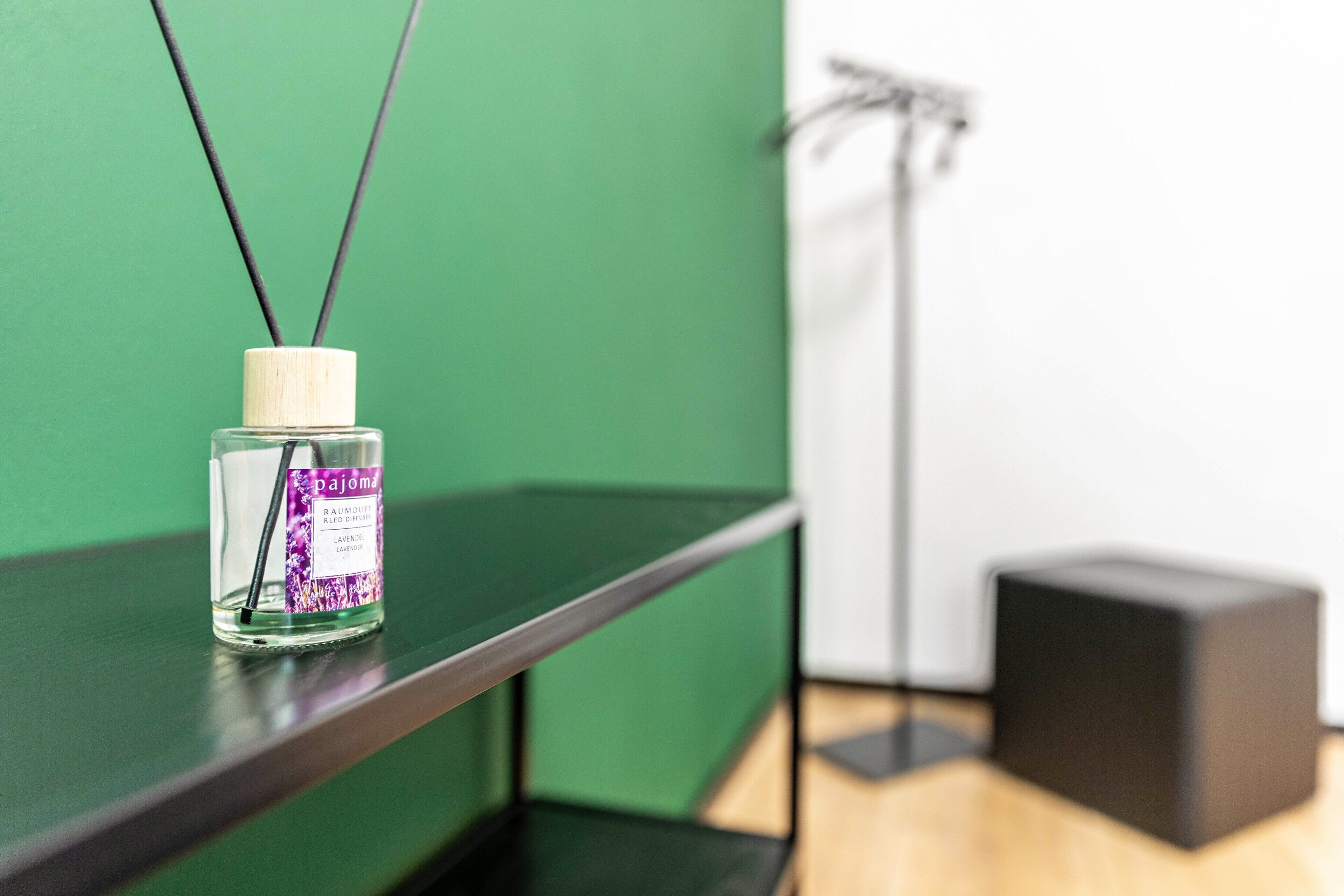 A clear bottle with a label on a shelf against a green wall.