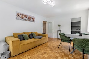 Un soggiorno moderno con un divano, un tavolo da pranzo con sedie, una zona cucina e una porta che dà su un'altra stanza.