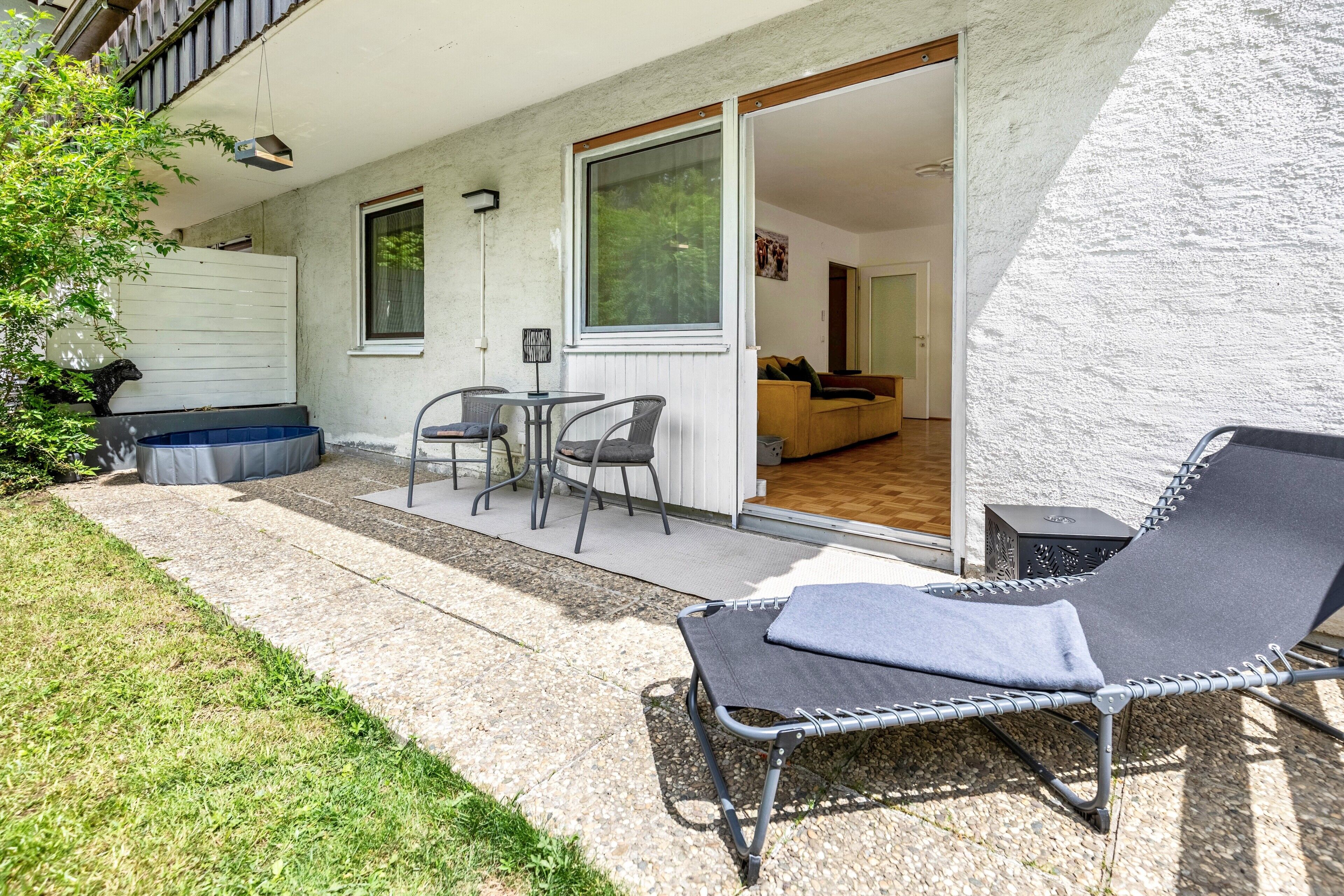 A patio with a lounge chair, a table with chairs, and a sliding glass door leading to an interior room.