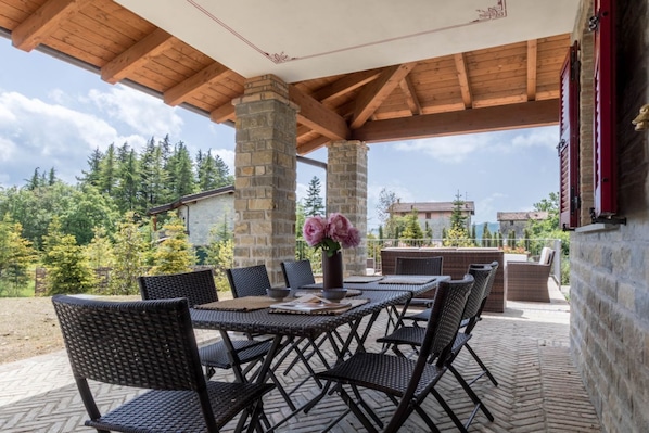 An outdoor patio with stone pillars, wicker furniture, and a view of the surrounding forest.