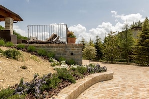 A stone patio with a curved brick border, a metal gate, and a small garden with various plants.