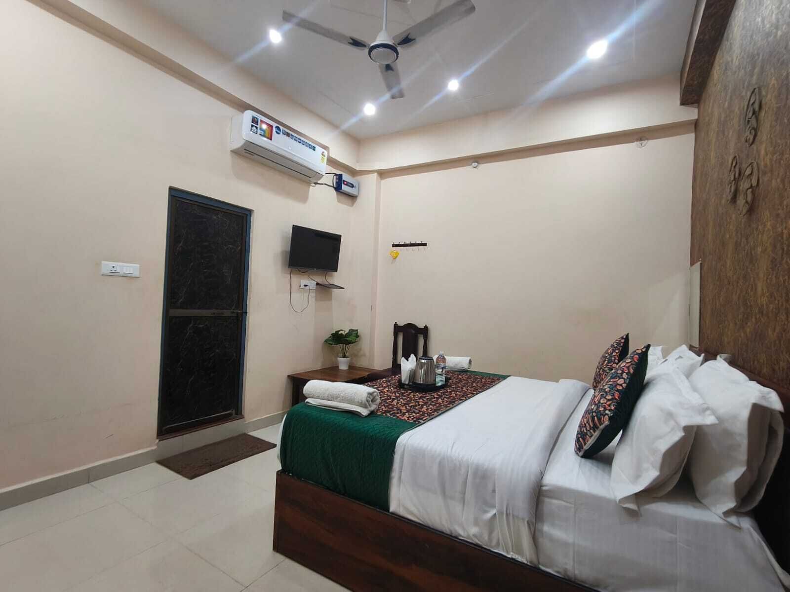 Un dormitorio con una cama, televisor, aire acondicionado, ventilador de techo y una puerta.