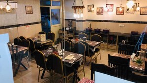 Un restaurante con varias mesas y sillas, una zona de cocina y diferentes lámparas colgantes.