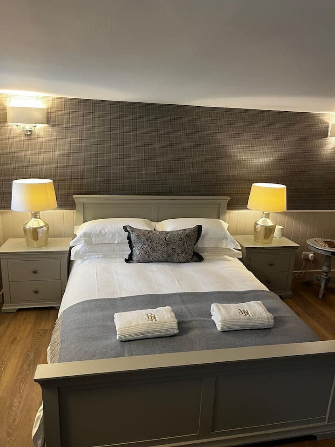 A hotel room with a large bed, two bedside tables with lamps, a nightstand, and a small round table.