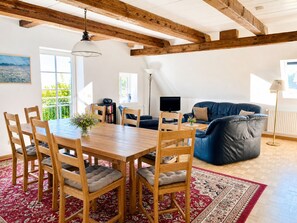 Ein Essbereich mit einem Holztisch, Stühlen, einem blauen Sofa und einem roten Teppich mit Muster.