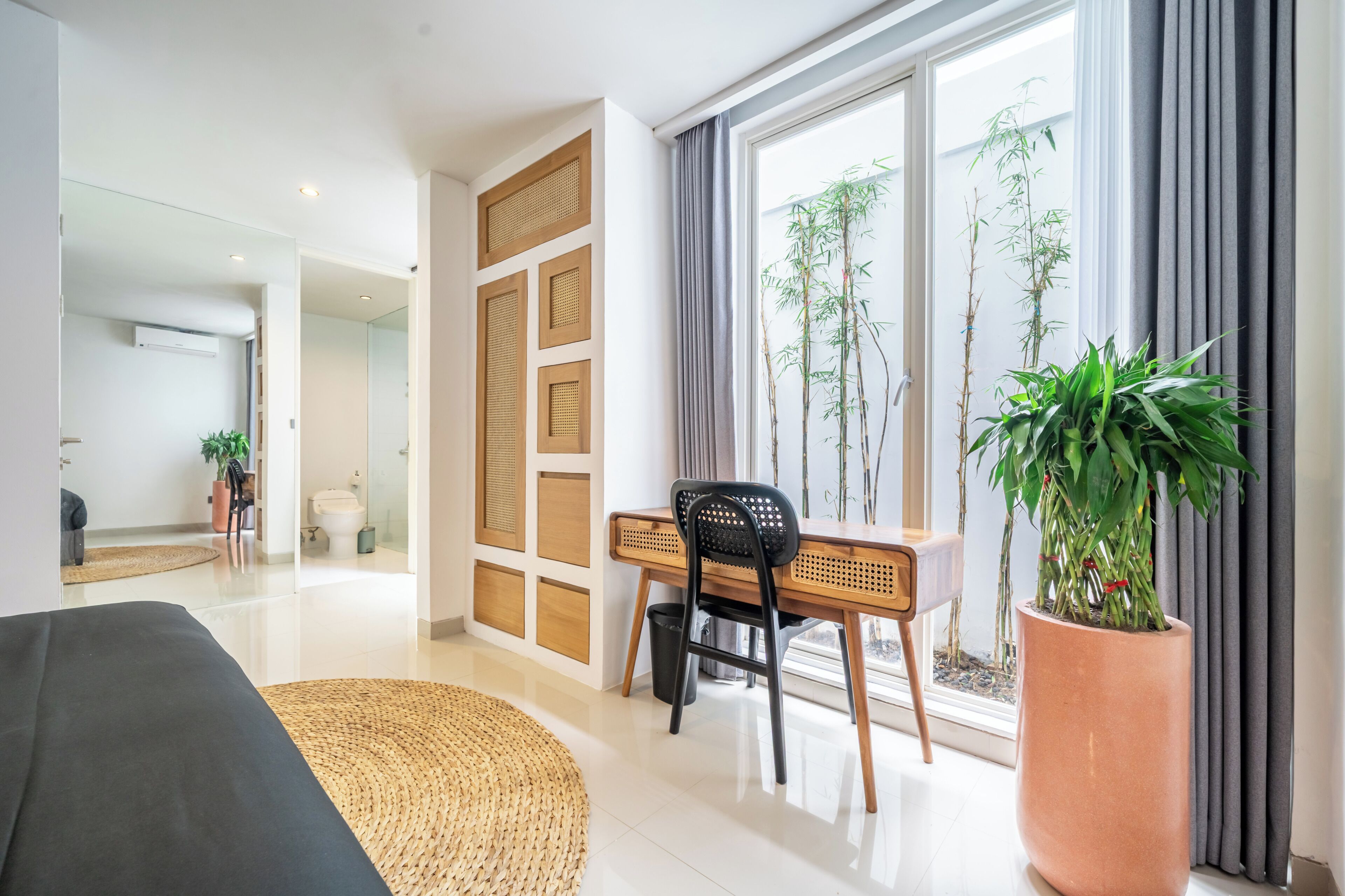 A modern living room with a large window, a desk, a chair, and a potted plant.