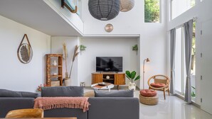 A modern living room with a flat-screen TV, grey sofas, a wooden cabinet, and a dining table. - Park Homei (Pecatu)