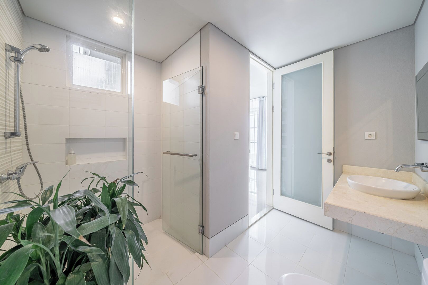 A modern bathroom with a glass shower enclosure, a sink with a marble countertop, and a potted plant.