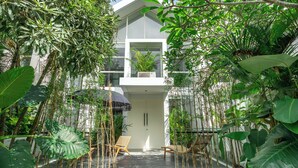A modern building with a balcony, surrounded by lush greenery and two wicker chairs. - Park Homei (Pecatu)
