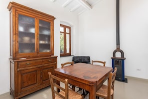 A dining area with a wooden table and chairs, a cabinet with glass doors, a fireplace, and a window with a view of greenery. - Casa con terrazza panoramica e servizio e-bike (Seneghe)