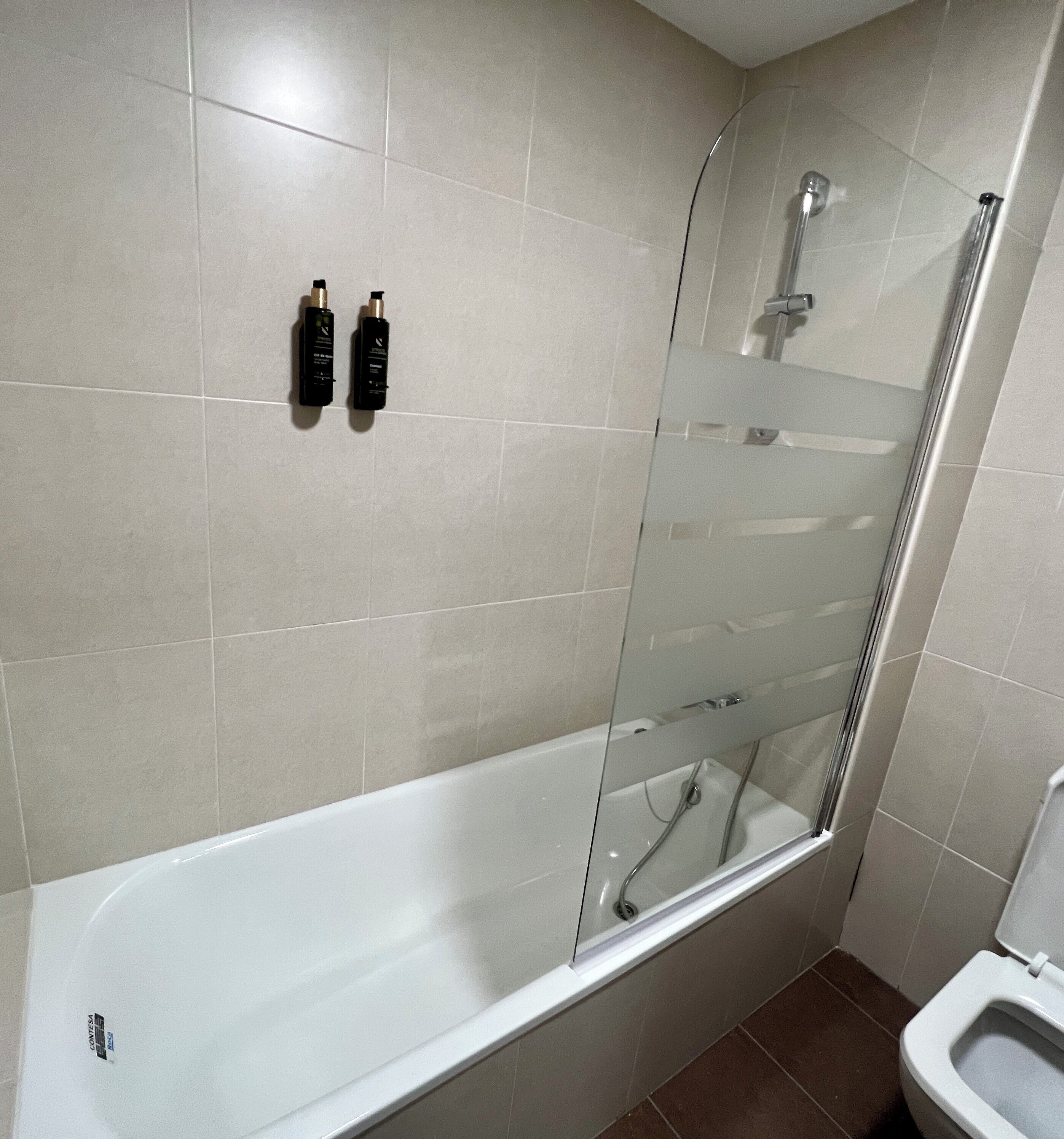 Ein modernes Badezimmer mit einer gläsernen Dusche, einer weißen Badewanne und zwei Pflegeprodukten an der Wand.