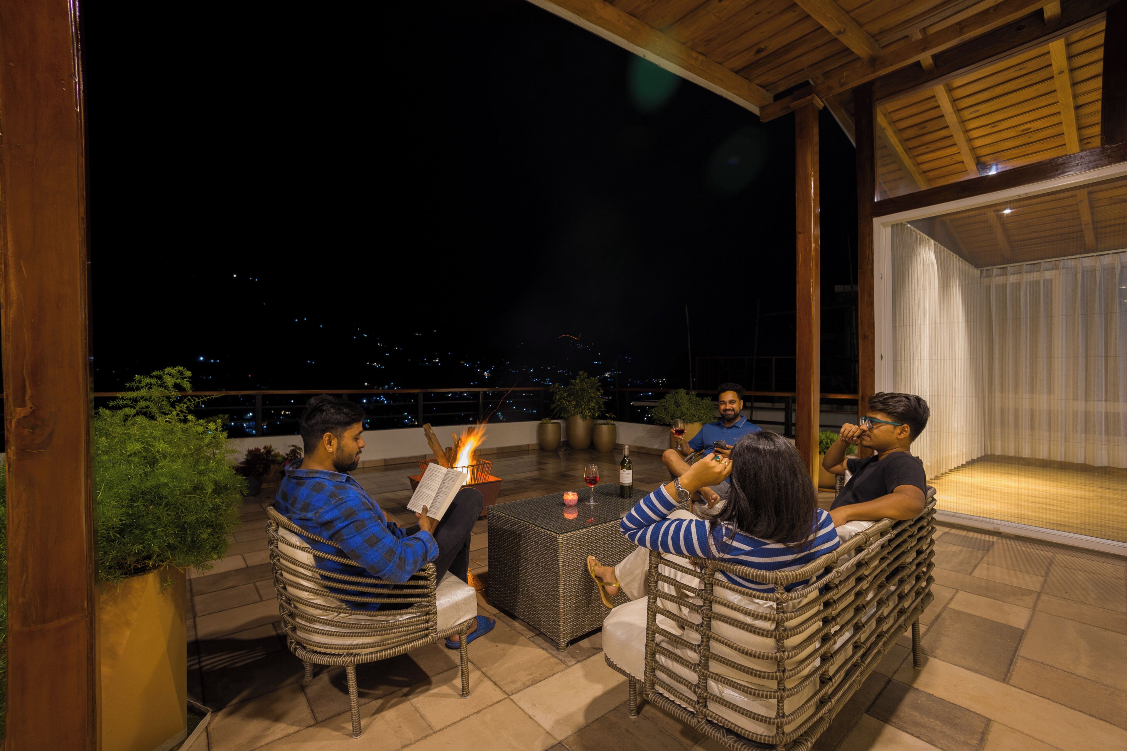 Une terrasse sur le toit, meublée de mobilier en osier, avec une table et une bougie, offrant une vue sur la ville la nuit.