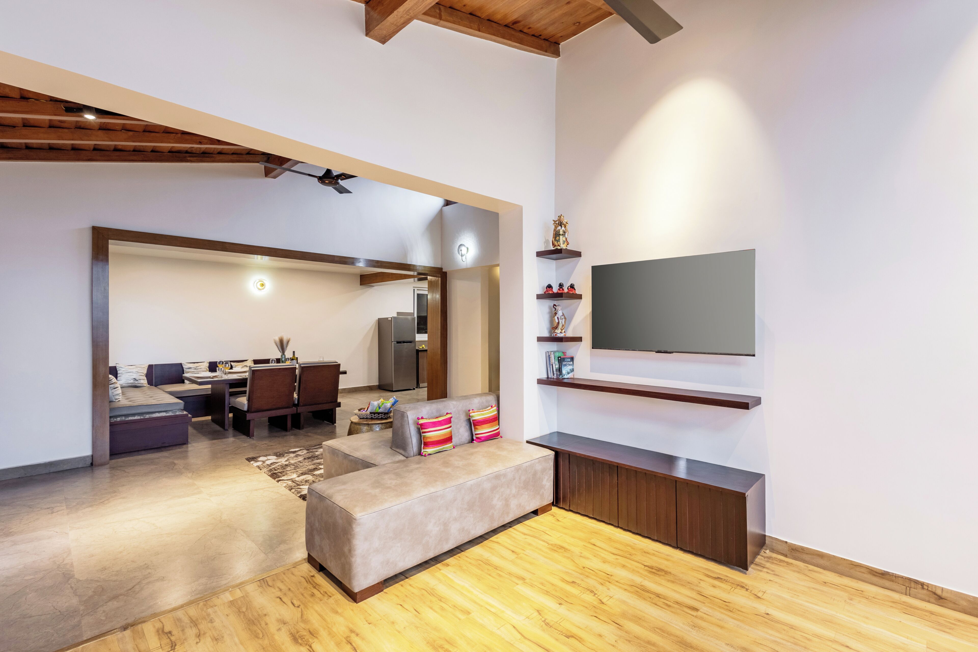 A modern living room with a sofa, a TV mounted on the wall, and a dining area in the background.