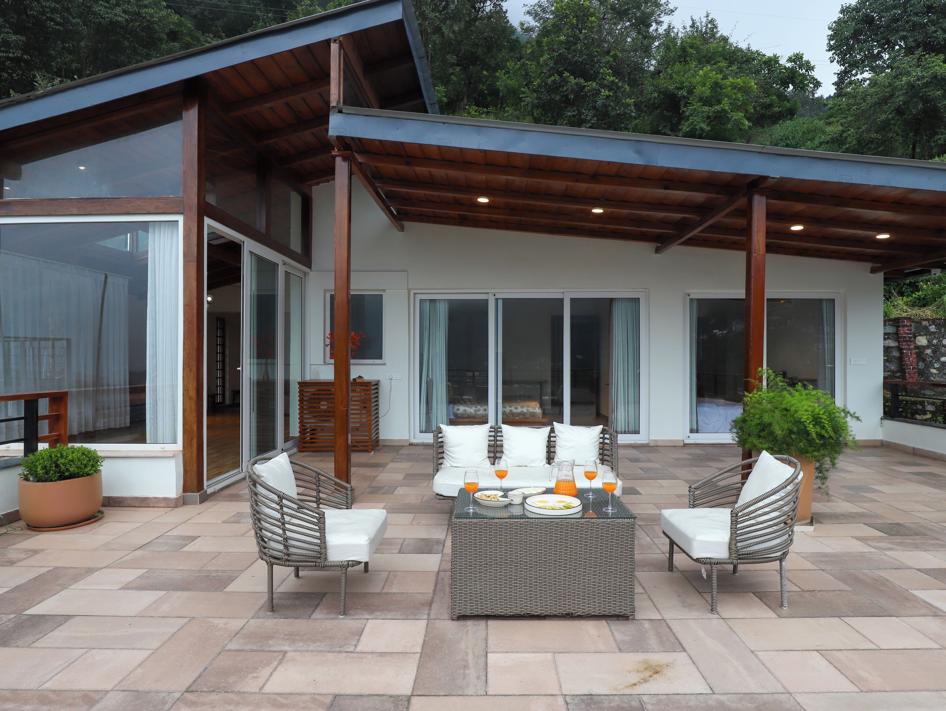 A modern outdoor patio with wicker furniture, a dining table with plates and glasses, and a potted plant.