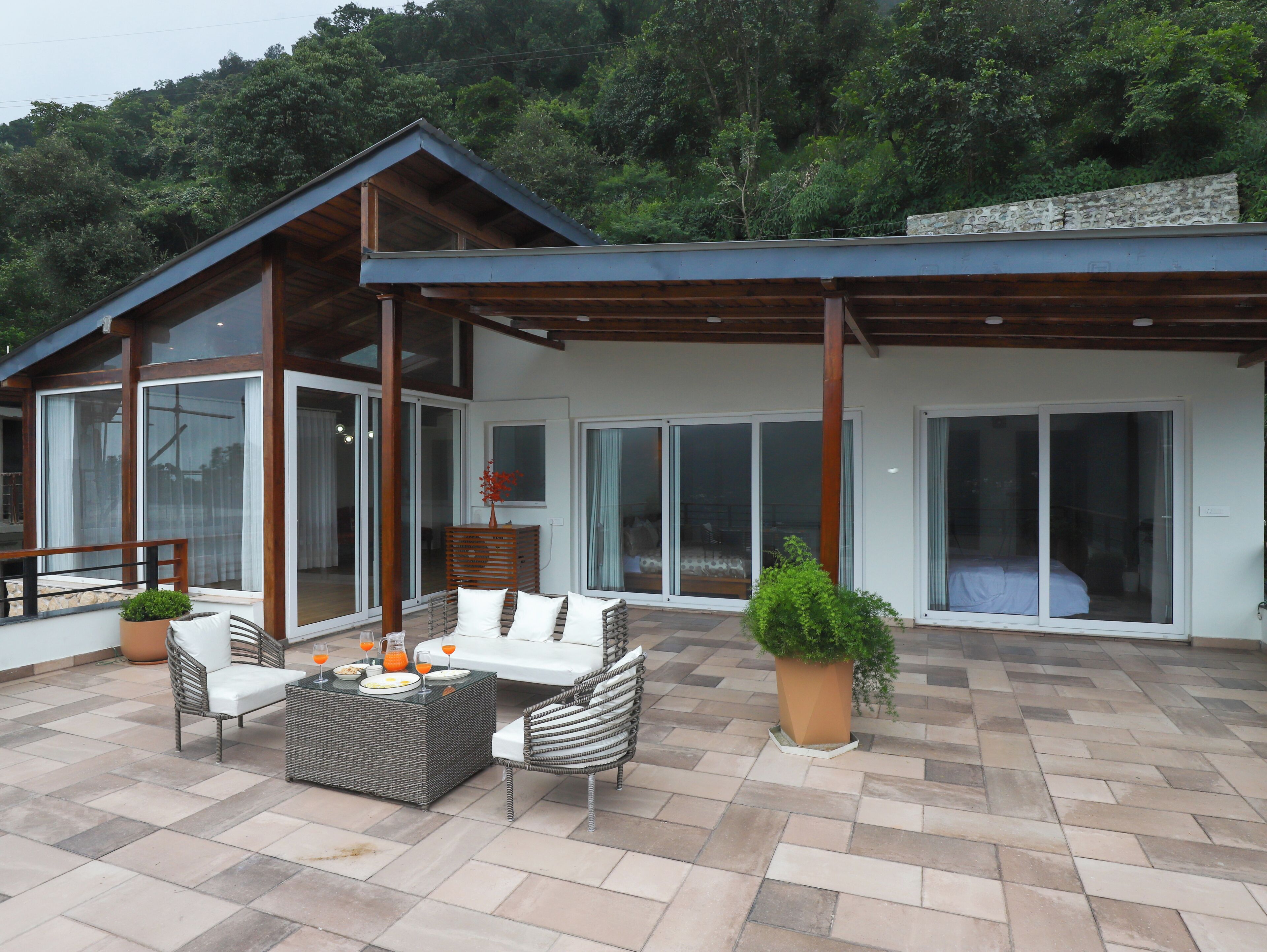 A modern house with a patio area featuring outdoor furniture, a dining table, and potted plants.