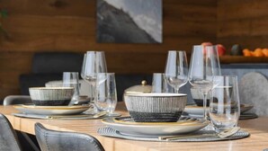 Una mesa de comedor dispuesta con platos, tazones y vasos, con una pintura de montaña al fondo.