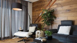 Un salón moderno con pared de madera, un sofá negro, un sillón negro, una mesita de centro redonda y una planta en maceta.