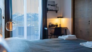 Habitación de hotel con cama, escritorio, silla, lámpara y vistas a las montañas desde la ventana.