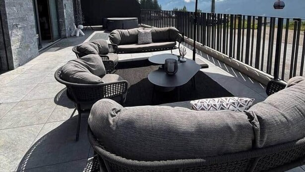 Un área de estar al aire libre con sofá, sillones, una mesa, un paraguas grande y vistas a montañas.