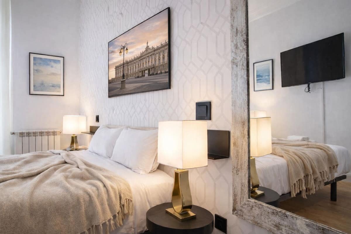 Ein Hotelzimmer mit einem großen Bett, zwei Nachttischlampen, einem Spiegel und einem Gemälde eines Gebäudes.