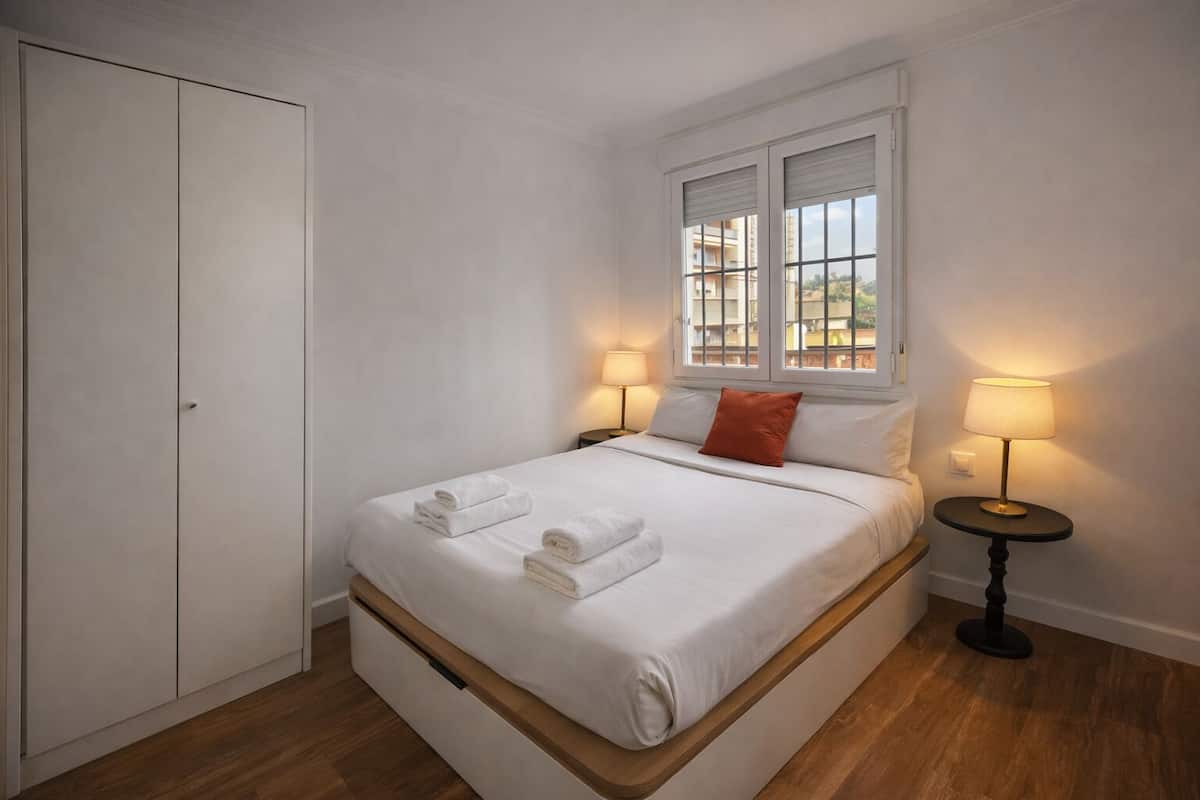 Ein Schlafzimmer mit einem Bett, zwei Nachttischlampen, einem Fenster und einem Kleiderschrank.