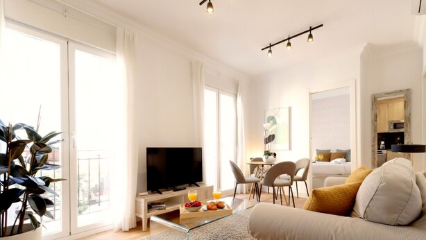 A modern living room with a flat-screen TV, a dining area with chairs, a kitchen area, and large windows. - Collection Madrid Rio (Madrid)