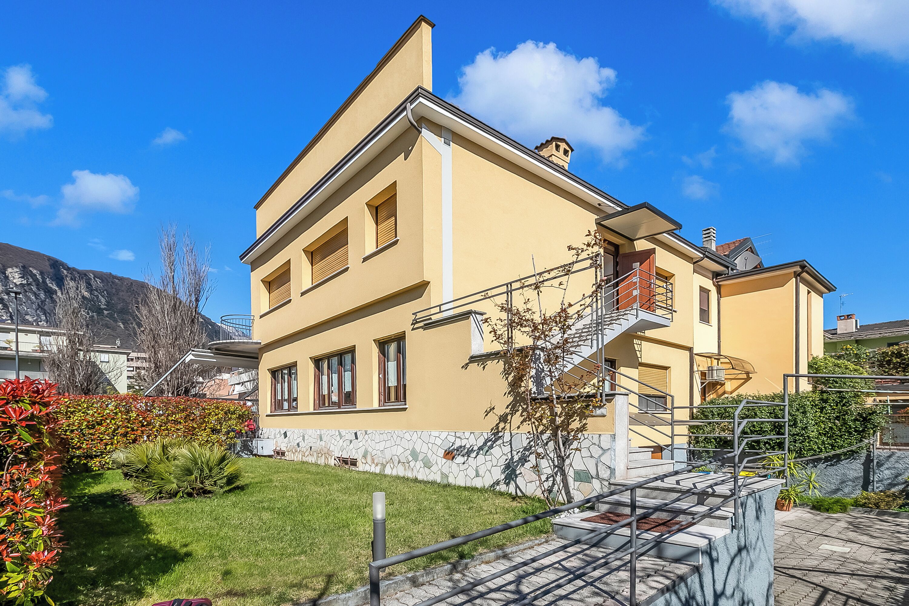 Ein zweistöckiges Gebäude mit Balkon, Treppe und einem mit Fliesen ausgelegten Garten.