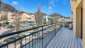 Un balcon donnant sur une rue, des immeubles et des montagnes.