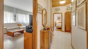 Un salon avec un canapé, une table basse et un téléviseur, un couloir orné de tableaux, et une chambre à coucher avec un lit.