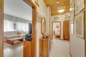 A living room with a sofa, coffee table, and TV, a hallway with framed pictures, and a bedroom with a bed. - Rosa Apartment, Balcony and AC (Riva del Garda)