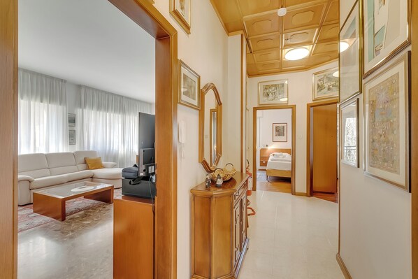 A living room with a sofa, coffee table, and TV, a hallway with framed pictures, and a bedroom with a bed. - Rosa Apartment, Balcony and AC (Riva del Garda)