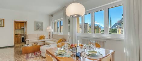 A modern living room with a dining area, large windows, and a view of mountains.